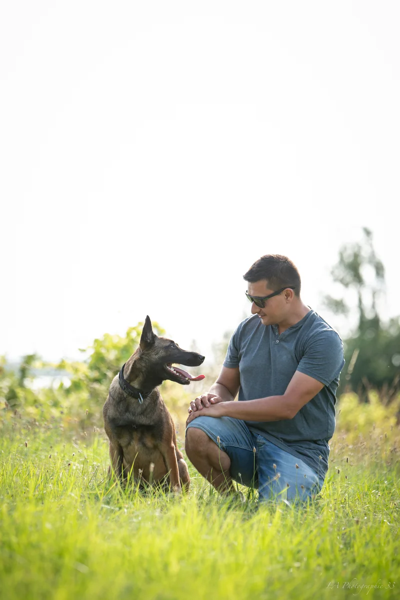 Homme accroupi souriant à son berger malinois dans un champ