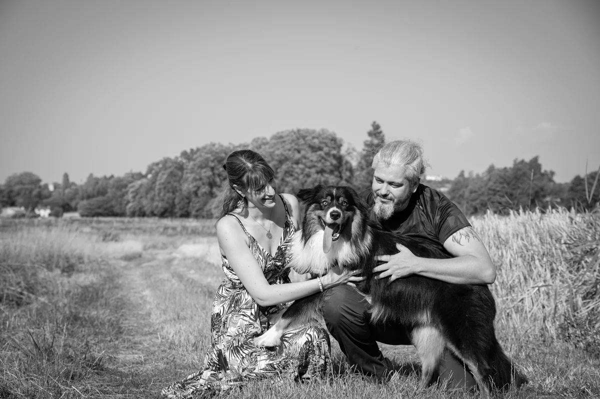 Photo en noir et blanc d'un couple caressant leur grand chien à poils longs dans un champ