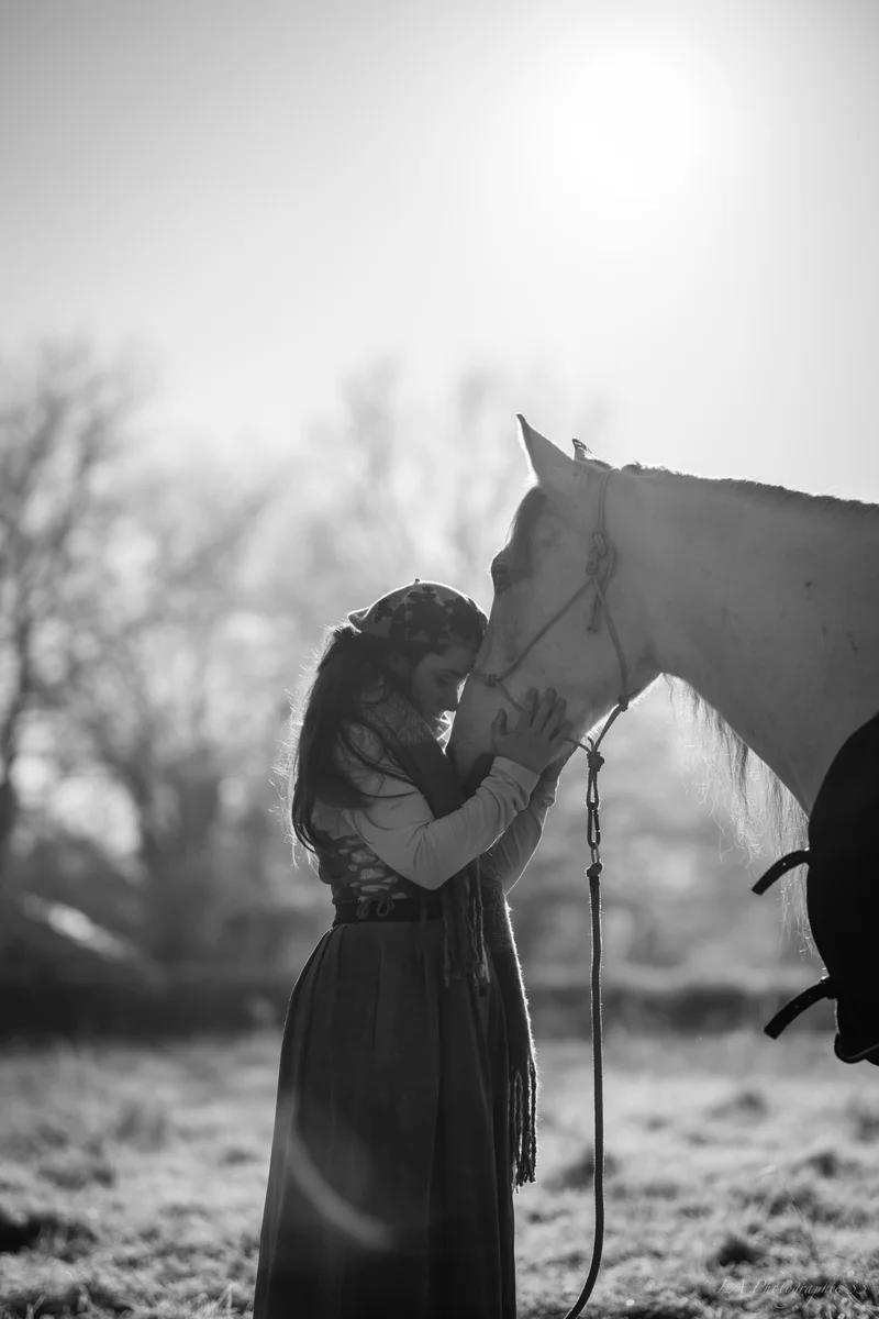 Photo en noir et blanc d'une jeune femme front contre front avec son cheval blanc