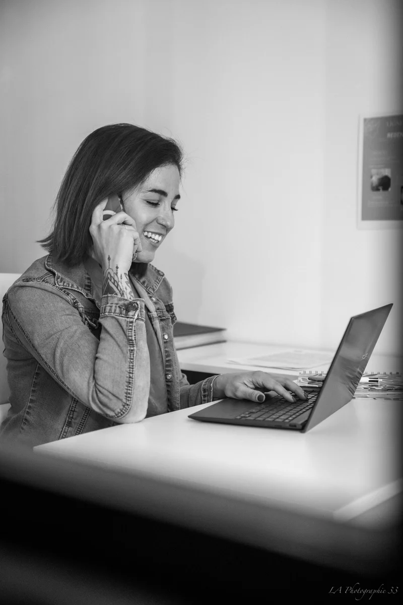 Femme souriante parlant au téléphone tout en travaillant sur un ordinateur portable, photo en noir et blanc