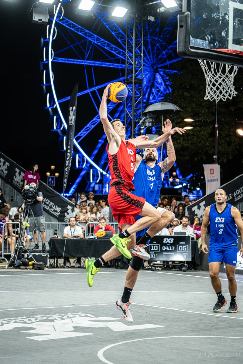 Joueurs de basket 3x3 en duel aérien pour un rebond sous un panier illuminé
