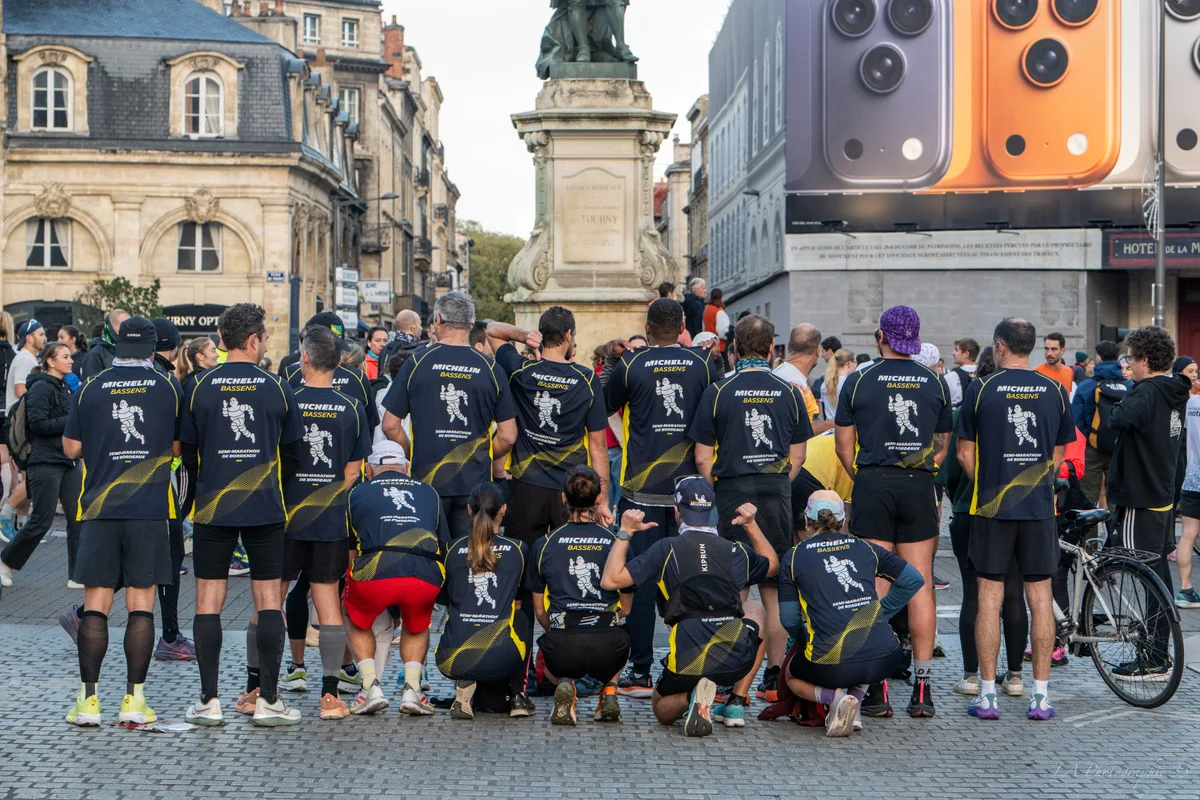 Groupe de coureurs portant des maillots 'Michelin Bassens' de dos, rassemblés avant le départ du Semi-Marathon de Bordeaux