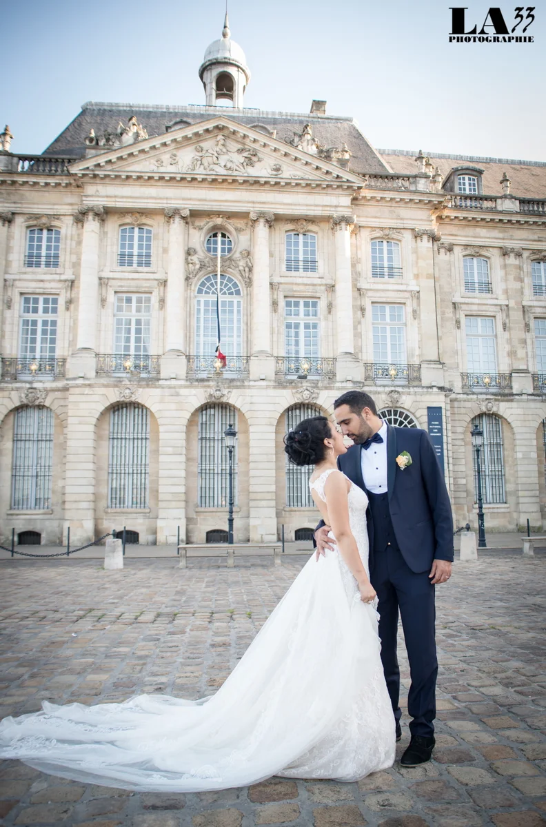 Couple de mariés s'embrassant devant la façade classique de la mairie de Bordeaux