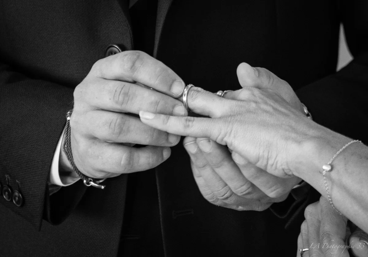 Gros plan en noir et blanc de deux mains lors de l'échange des alliances durant une cérémonie de mariage