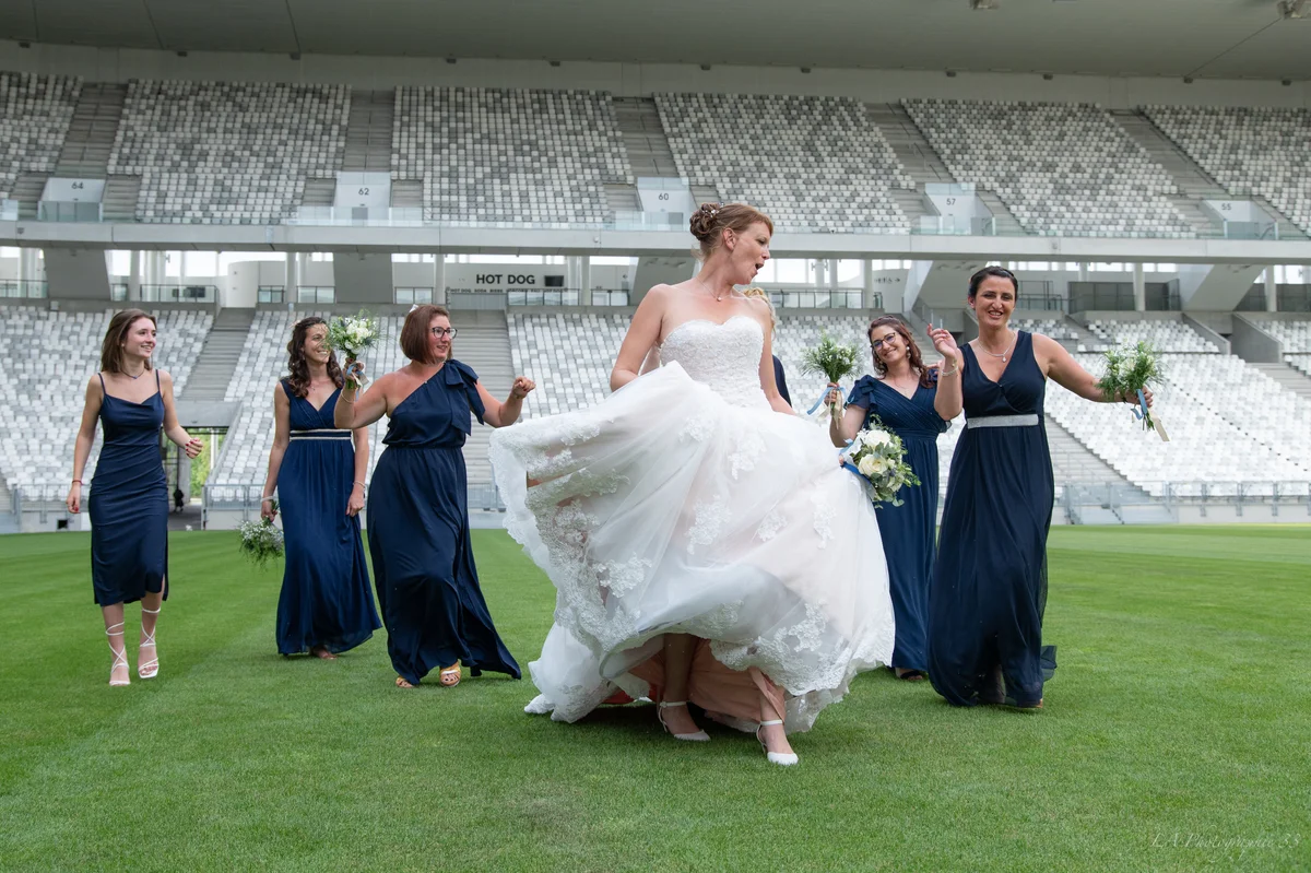Mariée souriante marchant sur la pelouse d'un stade entourée de ses demoiselles d'honneur en robes bleu marine