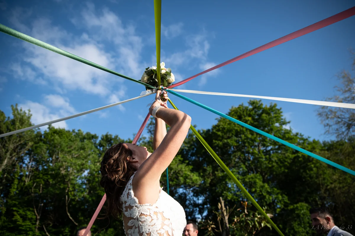 Mariée levant son bouquet relié à des rubans multicolores tendus vers le ciel