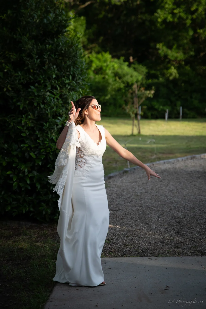 Mariée en lunettes de soleil ajustant son voile en dentelle dans un jardin