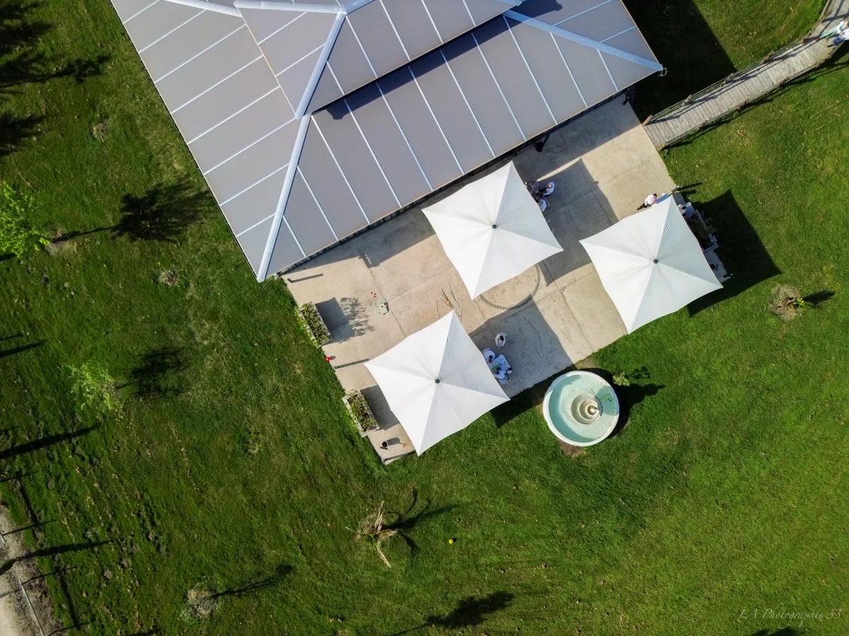 Vue aérienne à la verticale d'une terrasse de réception avec voiles d'ombrage triangulaires et fontaine
