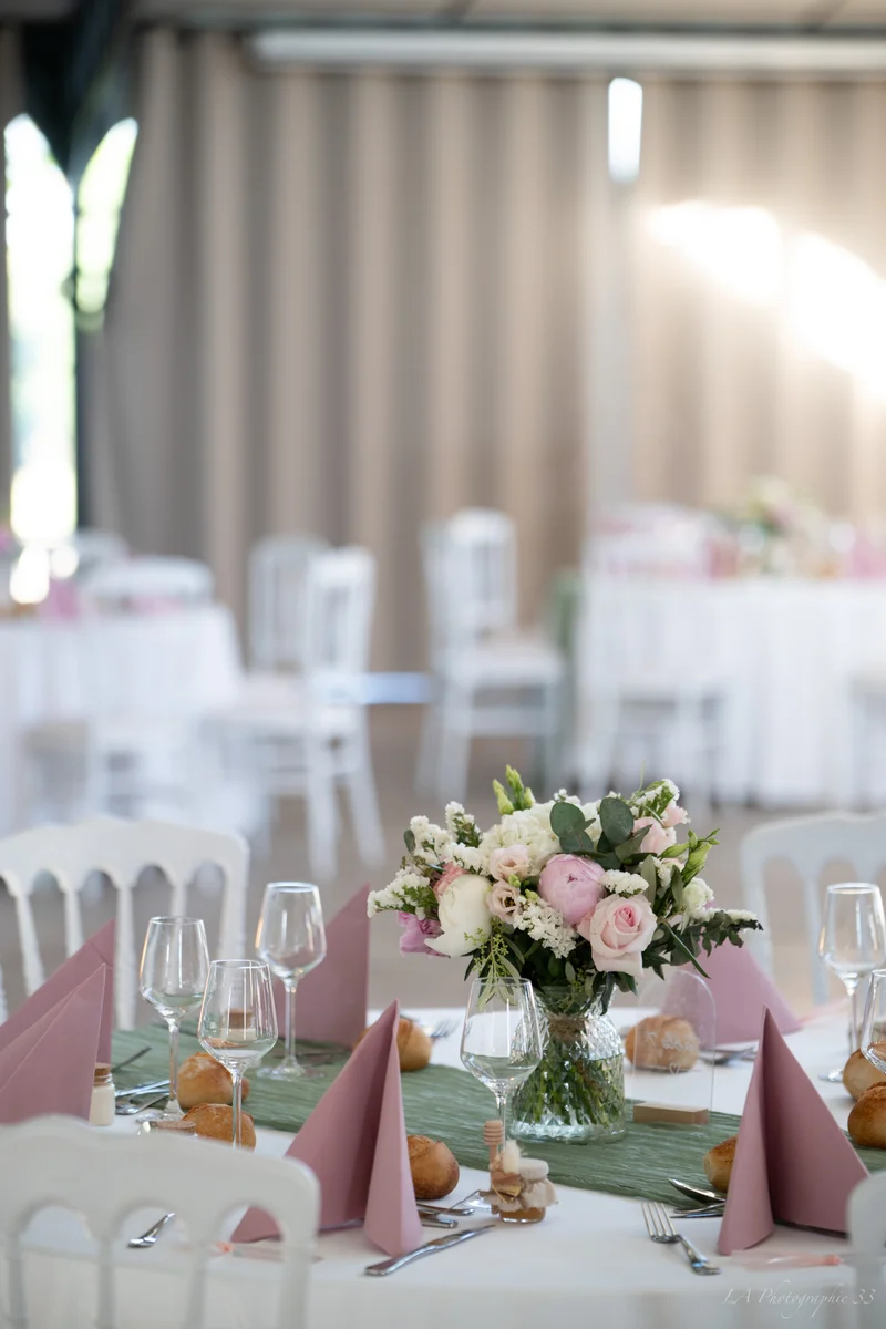 Table de réception dressée avec bouquet de fleurs roses et blanches, serviettes roses pliées et petits pains