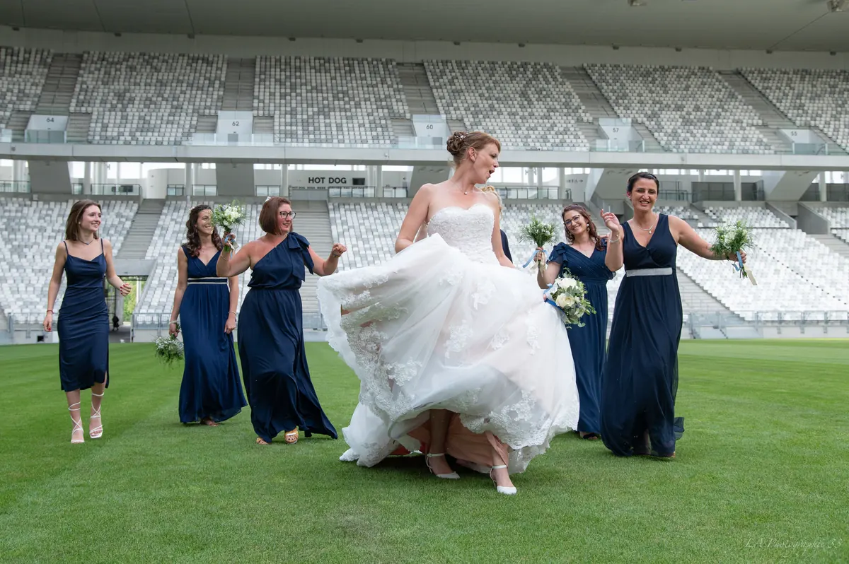 Mariée entourée de ses demoiselles d'honneur en robes bleu marine, marchant sur la pelouse d'un stade