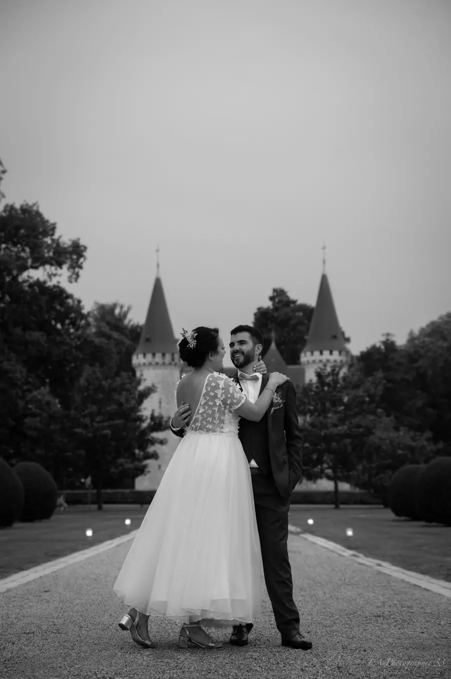 Les mariés enlacés de dos, photo en noir et blanc, château en arrière-plan