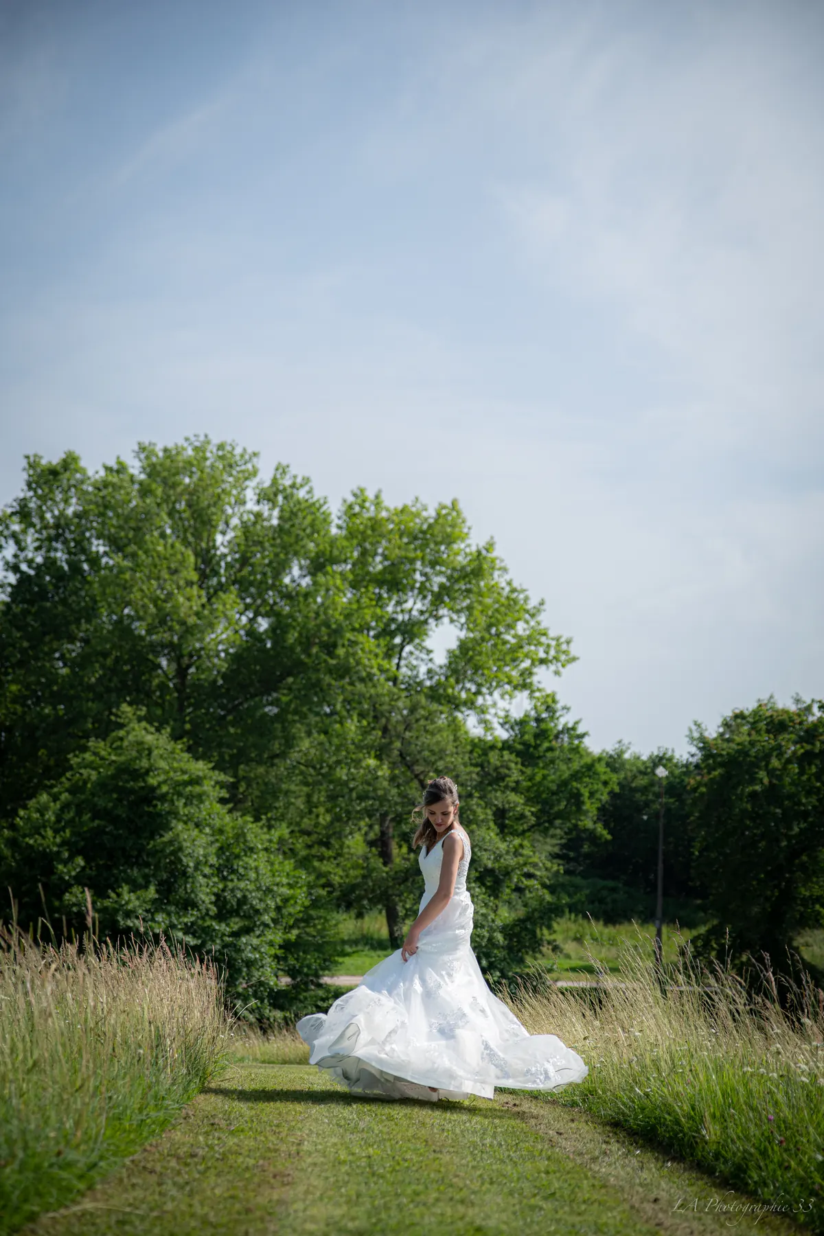 La mariée fait tourbillonner sa robe dans un champ, arbres et ciel en arrière-plan