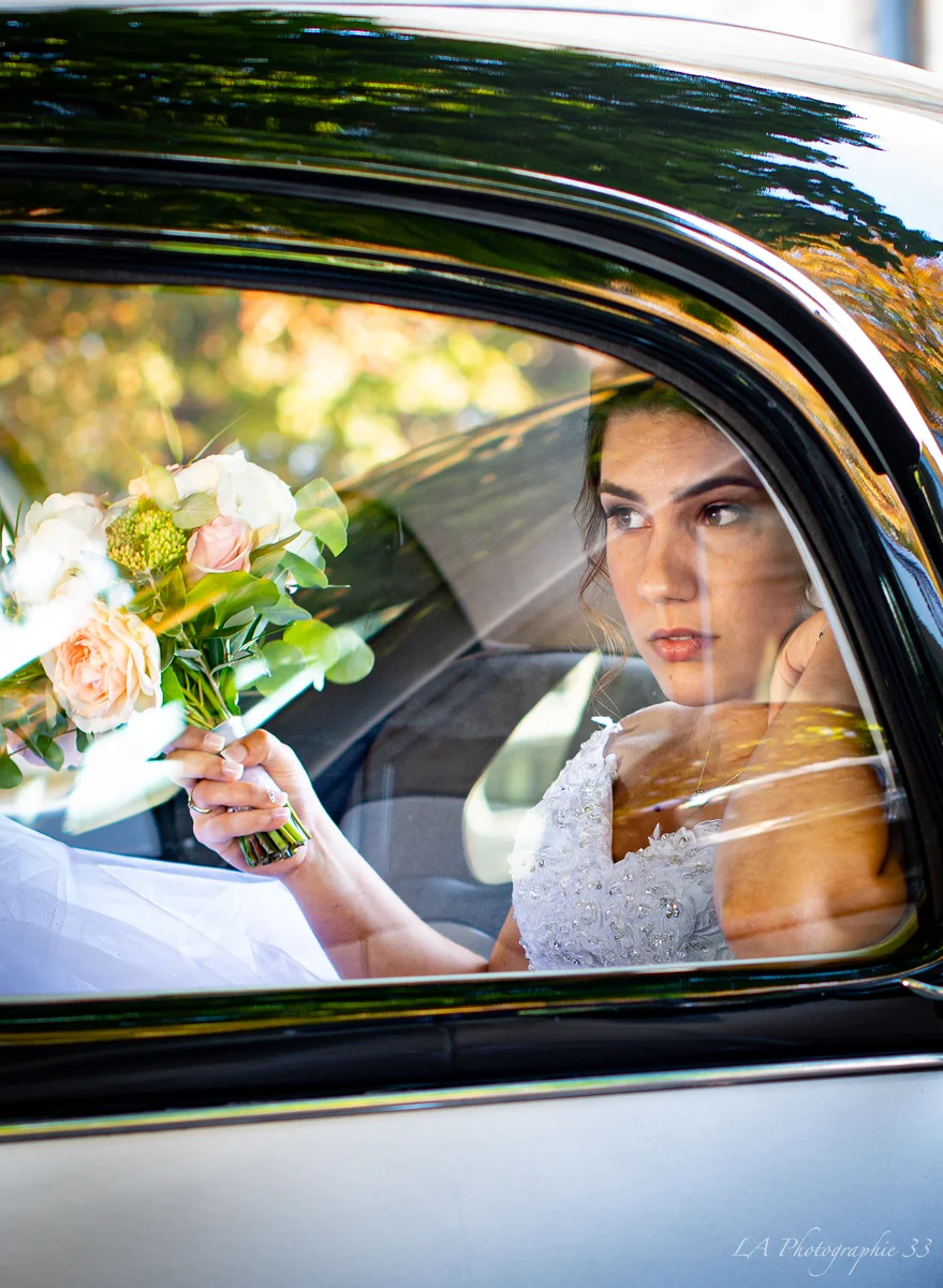 Mariée vue à travers la vitre d'une voiture, tenant un bouquet de roses blanches et roses