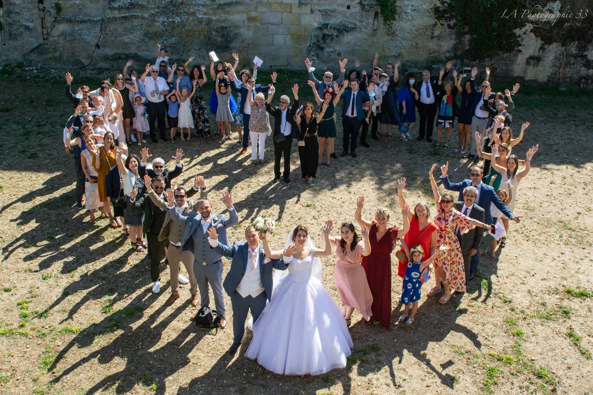 Photo aérienne des mariés entourés de leurs invités les bras levés, cour d'un château