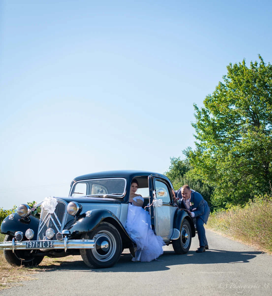 Mariés dans une voiture ancienne décorée, le marié aidant la mariée à sortir