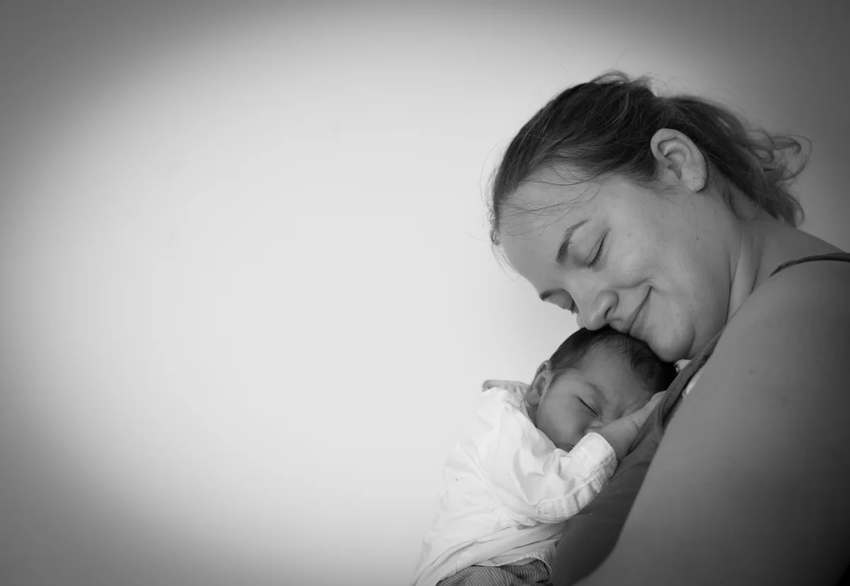 Photo en noir et blanc d'une mère tenant son nouveau-né endormi contre elle