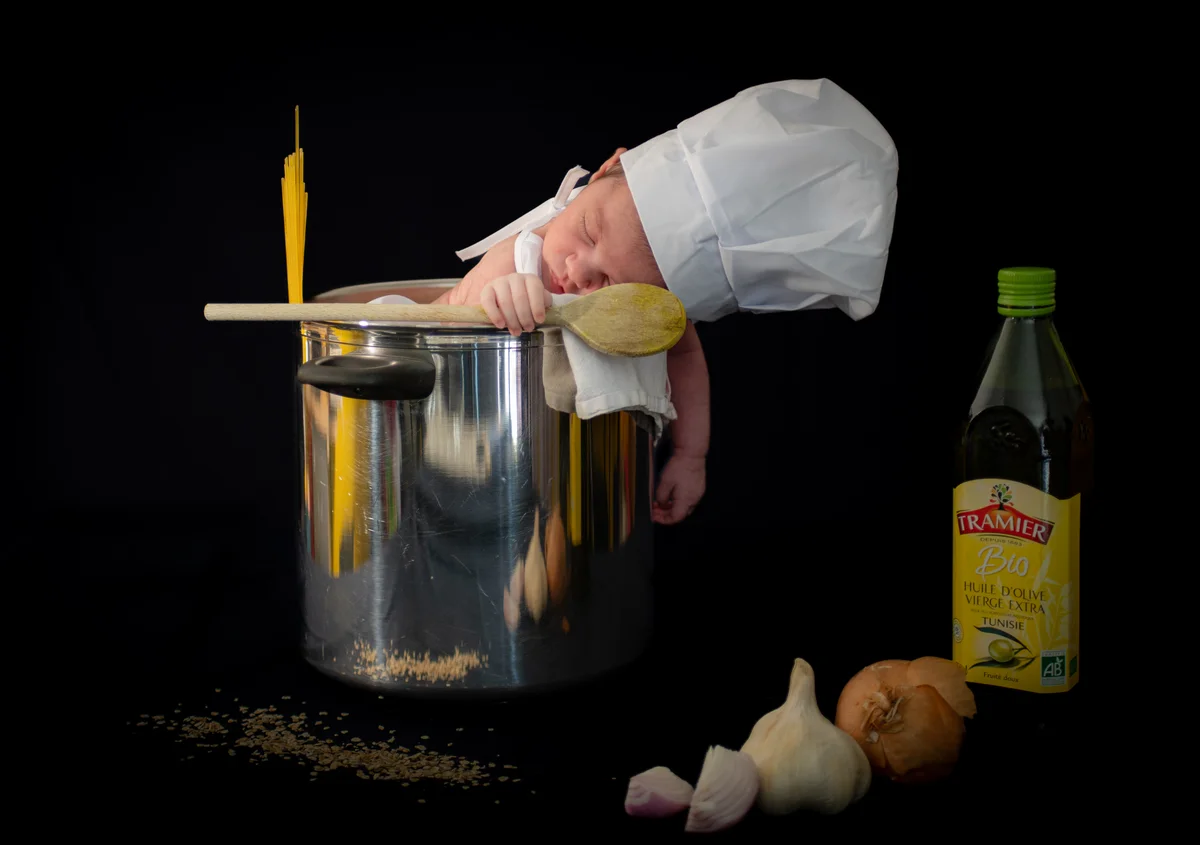 Nouveau-né endormi déguisé en petit chef cuisinier dans une marmite, mise en scène gourmande