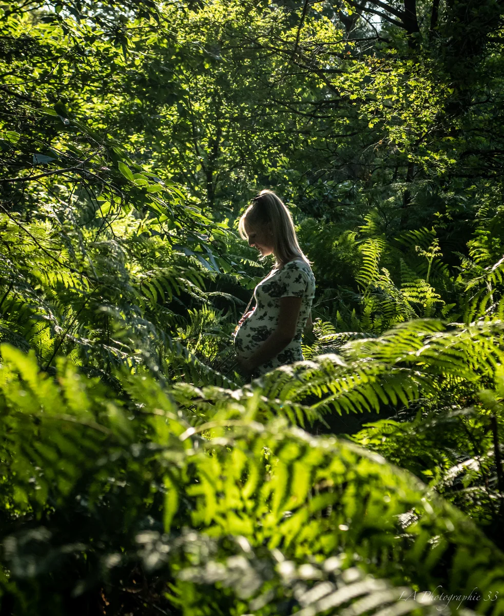 Femme enceinte de profil dans une forêt de fougères verdoyantes, éclairée par la lumière naturelle