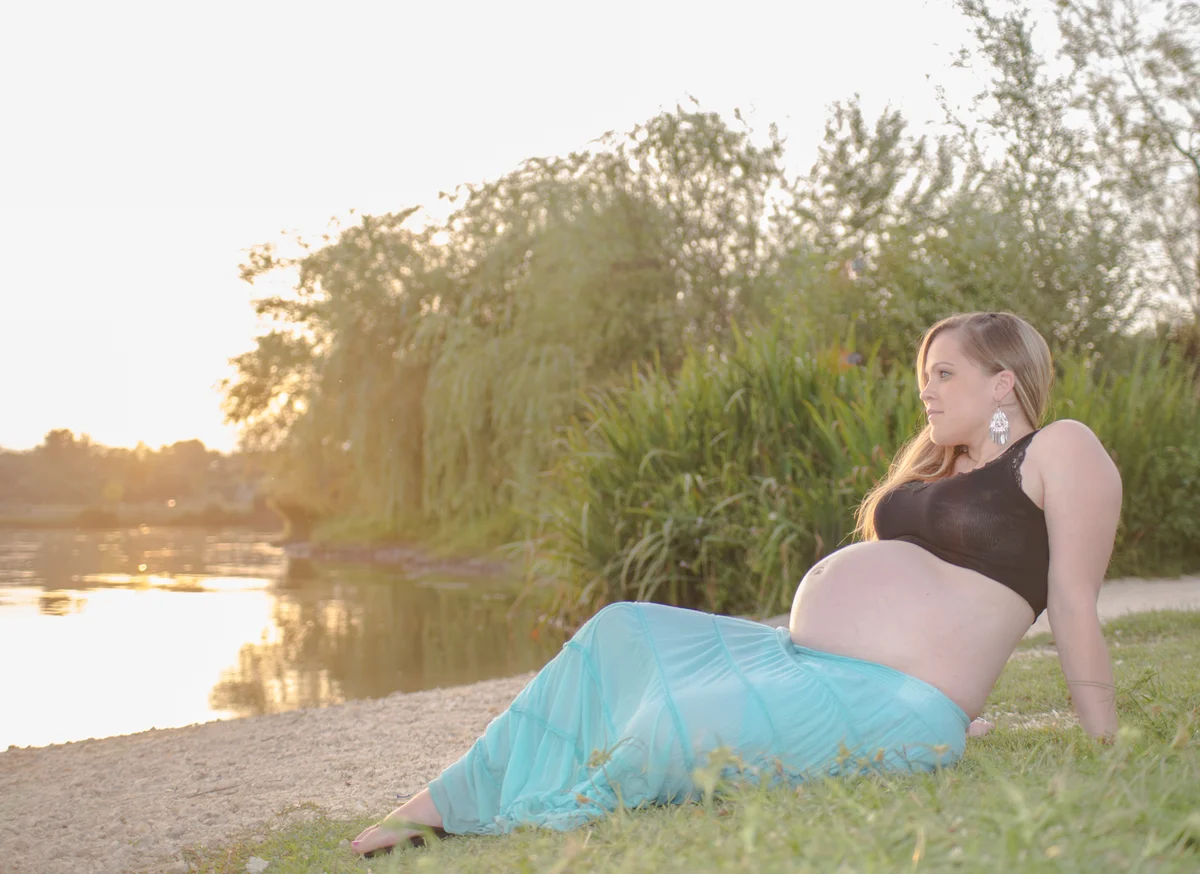 Femme enceinte allongée dans l'herbe au bord de l'eau au coucher de soleil