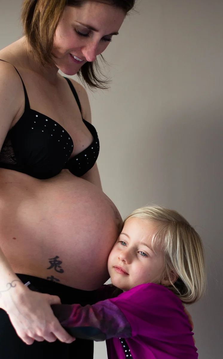 Femme enceinte souriante, sa petite fille blonde posant la tête contre son ventre