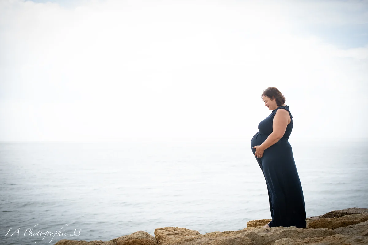 Femme enceinte de profil en robe bleu marine face à la mer