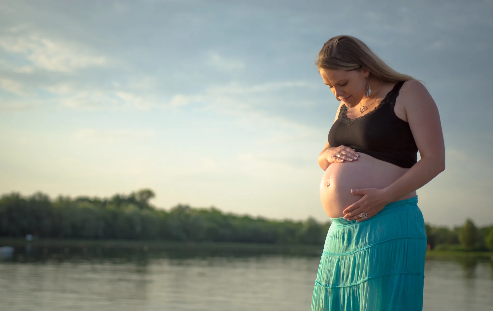 Séance maternité, femme enceinte au bord d'un lac au coucher du soleil
