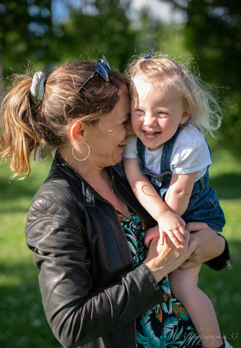 Mère souriant joue contre joue avec son jeune enfant hilare, en extérieur dans un jardin