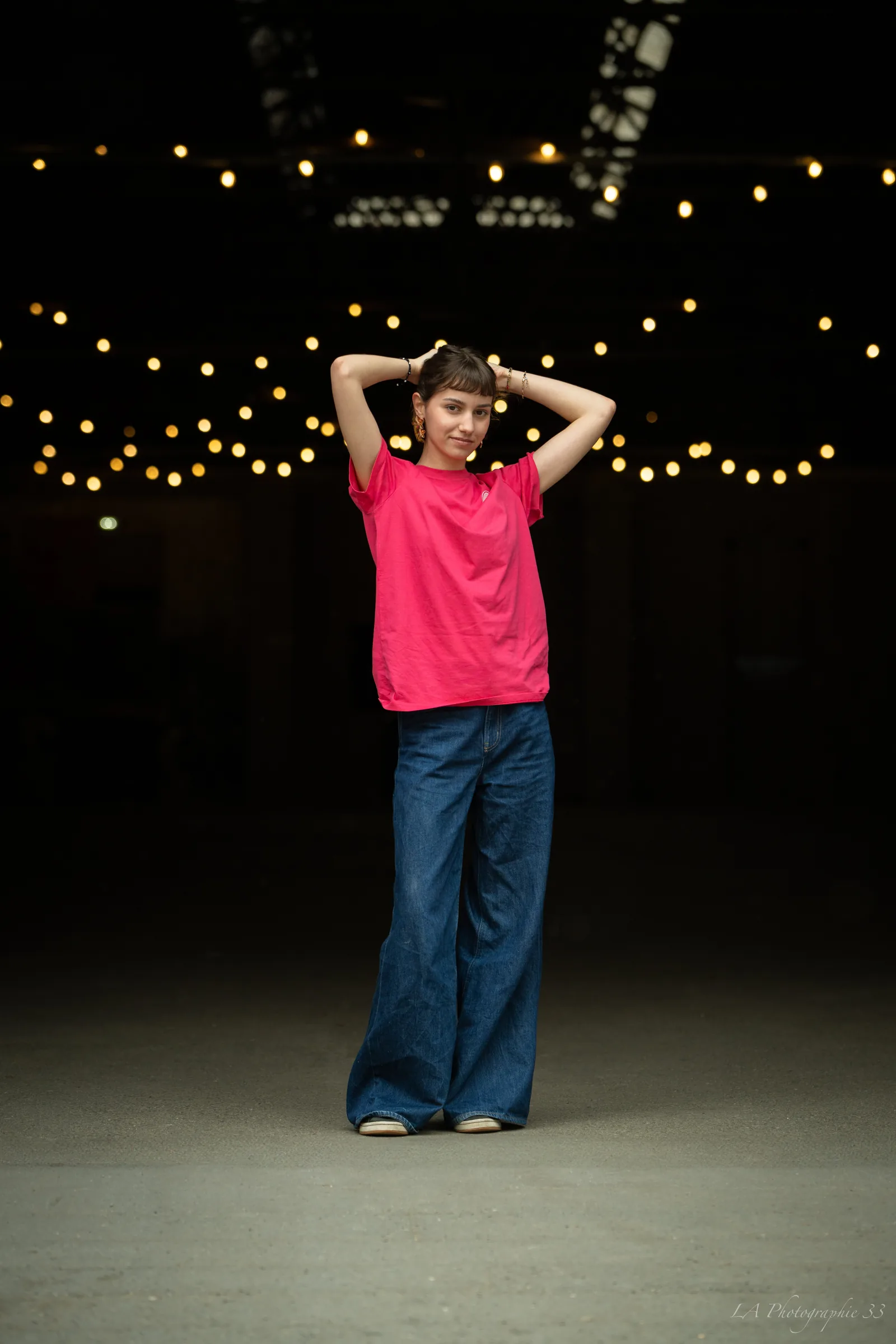 Jeune femme en tee-shirt rose posant de nuit sous une guirlande lumineuse