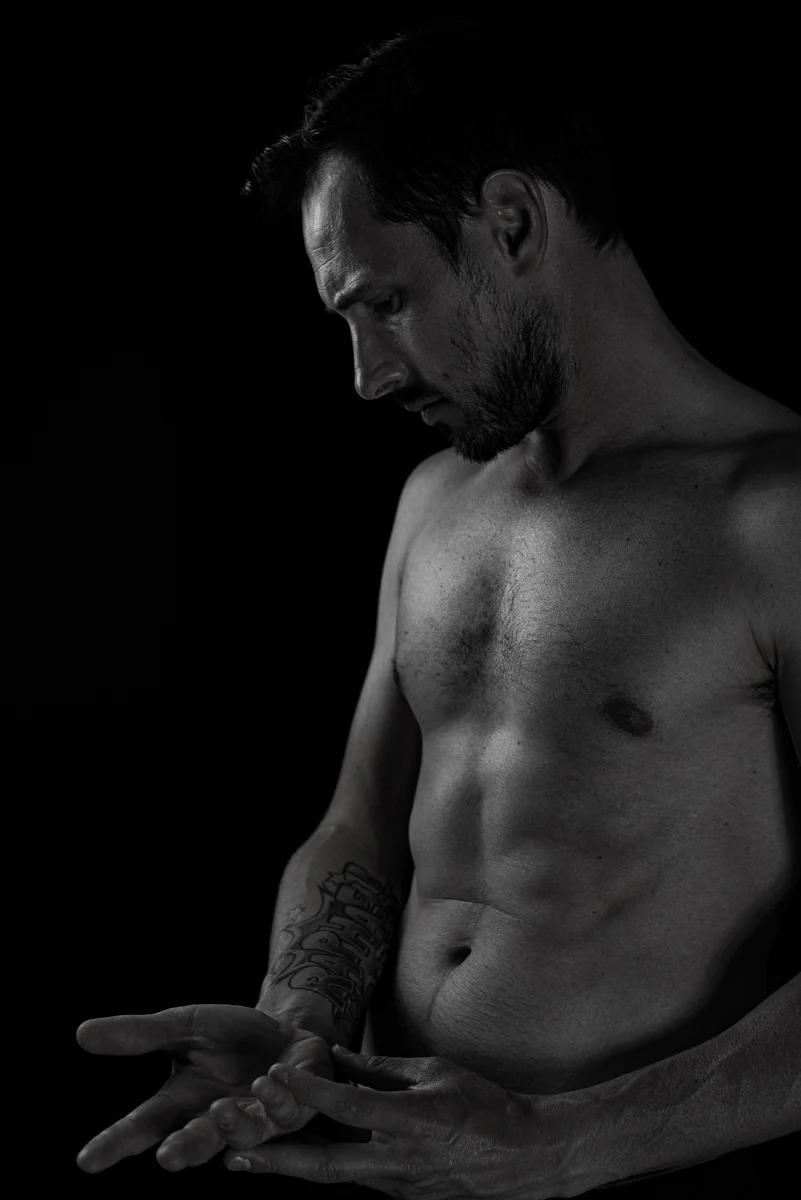 Portrait en noir et blanc d'un homme torse nu de profil, fond sombre